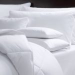 The corner of a hotel bed featuring a variety of pillows and a LuxSoft hotel blanket comforter.