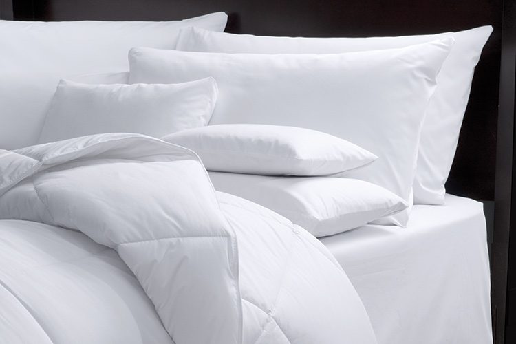 The corner of a hotel bed featuring a variety of pillows and a LuxSoft hotel blanket comforter.
