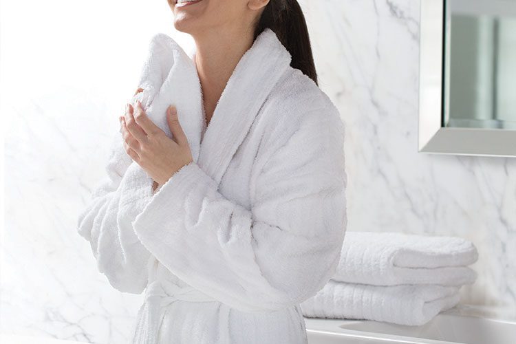 A woman standing in a hotel bathroom wearing a Luxury Stripe Robe.