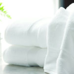 A Lynova bath towel draped over a stack of two folded Lynova bath towels.