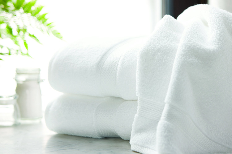 A Lynova bath towel draped over a stack of two folded Lynova bath towels.