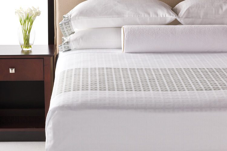 A detail shot of a hotel bed featuring a top cover with integrated bed scarf with our block-on-block pattern and songbird color option.