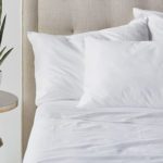 Hotel bed with three pillows and Paragon Cotton sheets next to a plant on a nightstand