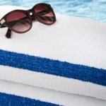 A pair of sunglasses sits atop a stack of two classic Stripe Pool Towels.