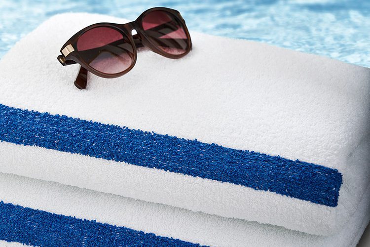 A pair of sunglasses sits atop a stack of two classic Stripe Pool Towels.