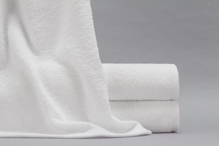 A Gradient bath towel draped over a stack of two folded Gradient bath towels.