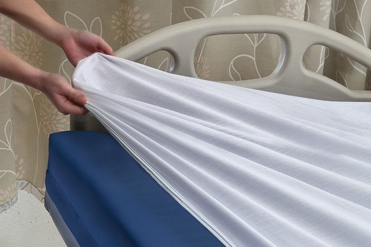 Two hands pulling a Versatility fitted sheet over a patient mattress.
