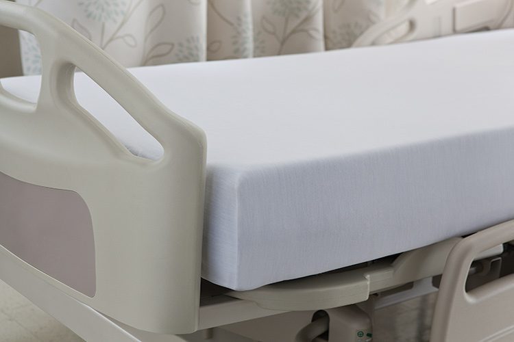 A close up shot of a patient bed with a Versatility fitted sheet over the mattress.