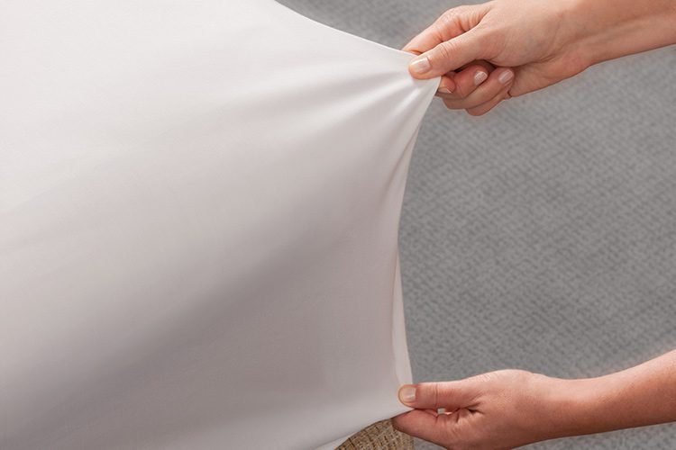 A close up an individual pulling Versatility fitted sheets onto a mattress.