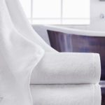 A Vidori towel draped delicately over a stack of two folded Vidori bath towels.