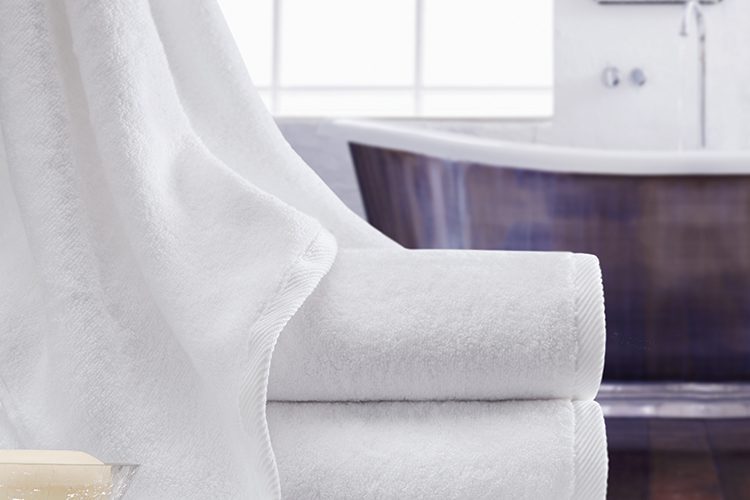 A Vidori towel draped delicately over a stack of two folded Vidori bath towels.