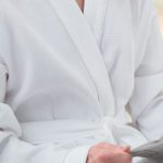 A person reading a newspaper while wearing a Waffle hotel robe.