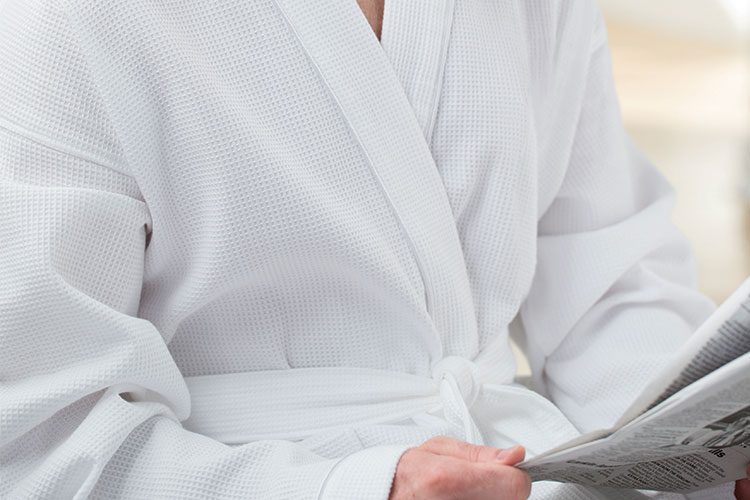 A person reading a newspaper while wearing a Waffle hotel robe.