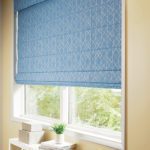 Photo of a blue roman shade hanging in a window.