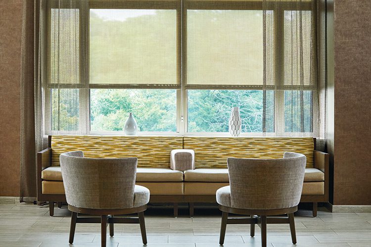 A seating area featuring a long couch and two chairs in front of a large window featuring manual solar shades.