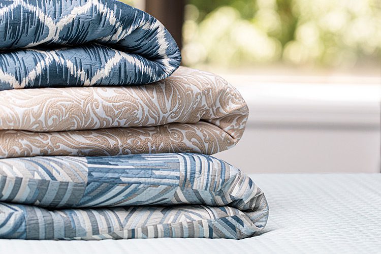 A stack of three folded bed spreads, each a unique color and pattern.