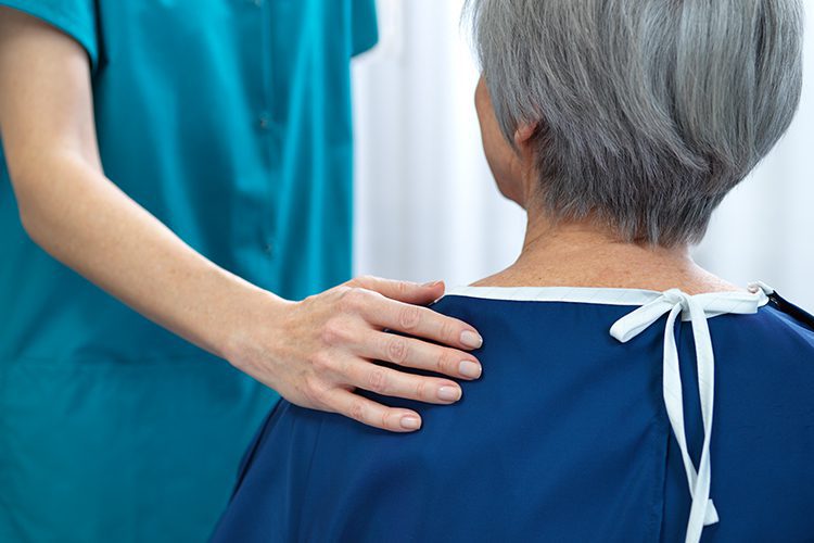 A nurse's hand rests on a patient's shoulder.