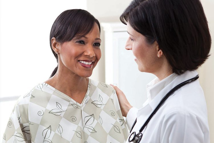 A patient wearing a reusable hospital gown is being comforted by her doctor. E*Star® medical gowns, shown in the Leaves pattern. Our hospital patient gowns offer a solution for patients, caregivers & medical teams, with clinically compatible access points, full coverage.