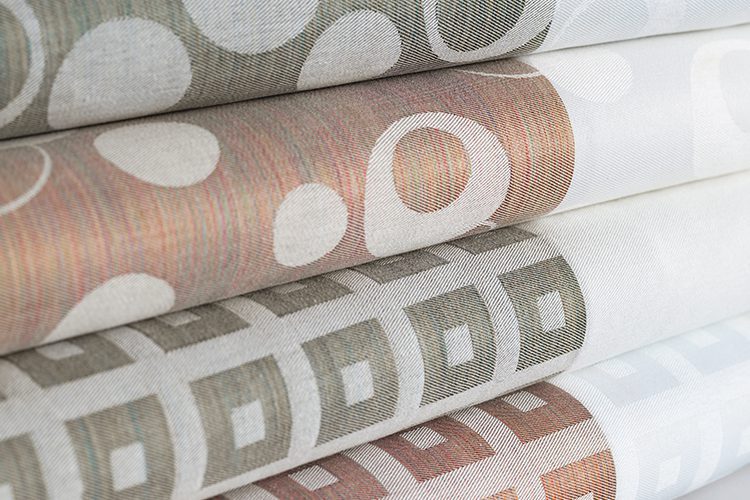 A folded stack of top covers with integrated bed scarfs. A variety of colors and patterns are shown.
