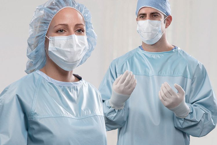 Two doctors prepping for surgery, wearing surgical gowns, masks, gloves, and hair protection.