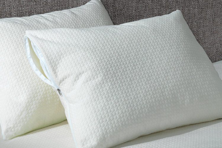 Two pillows encased in AllerEase Platinum pillow protectors leaning against a grey headboard sitting atop an allerease hotel mattress encasement