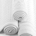 A stack of three rolled up Artesano bath rugs.