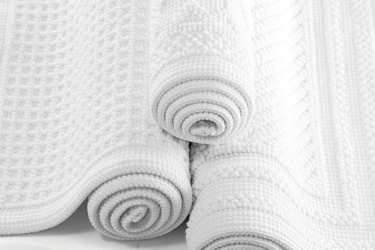A stack of three rolled up Artesano bath rugs.