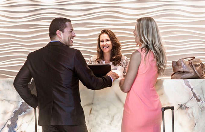 A well dressed couple standing before a receptionist at the check-in counter in a hotel lobby.