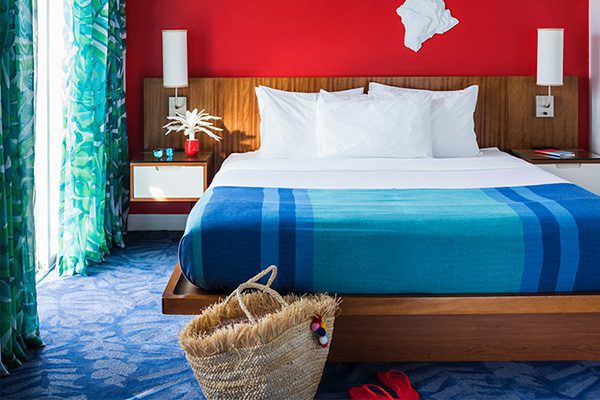 A colorful, bright hotel guest room, featuring a variety of vibrant colors and patterns from the bed, walls, and window treatments.
