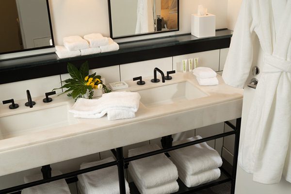 A modern, stylish guest bathroom featuring folded piles of fluffy towels and washcloths. A robe hangs nearby.
