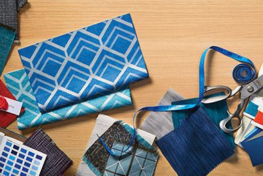 A variety of fabric samples and a pair of scissors lay on a wood grain surface.