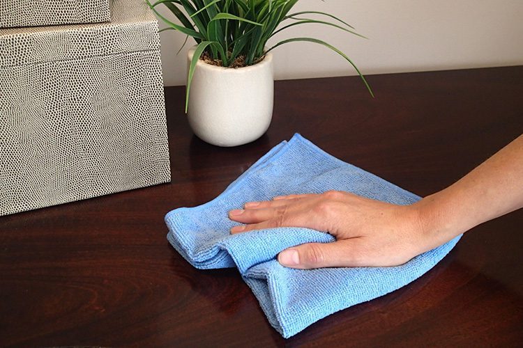 A hand using a microfiber cleaning cloth on a dark wood surface.