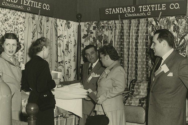 A vintage photo of a group of Standard Textile employees gathered in a fabric showroom.