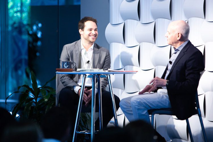 Alex Heiman and Gary Heiman seated at a table, having a conversation during a company presentation.