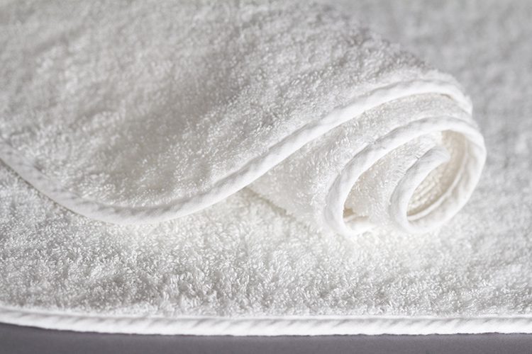 A rolled Remarkable Bath Rug lays on top of an unrolled bath rug.