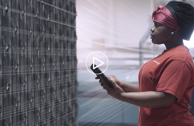 Image of an associate inspecting threads on a loom. There is a video icon overlaying the image. The image links to video about Smart Manufacturing.