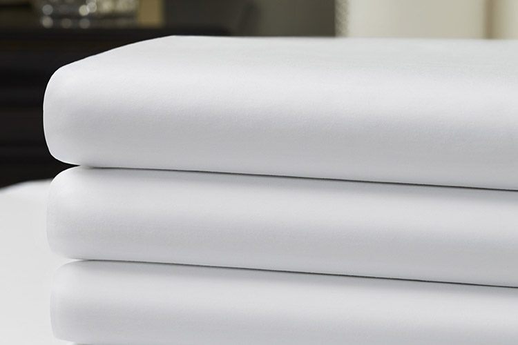Stack of three luxury Vidori sheets in a hotel room