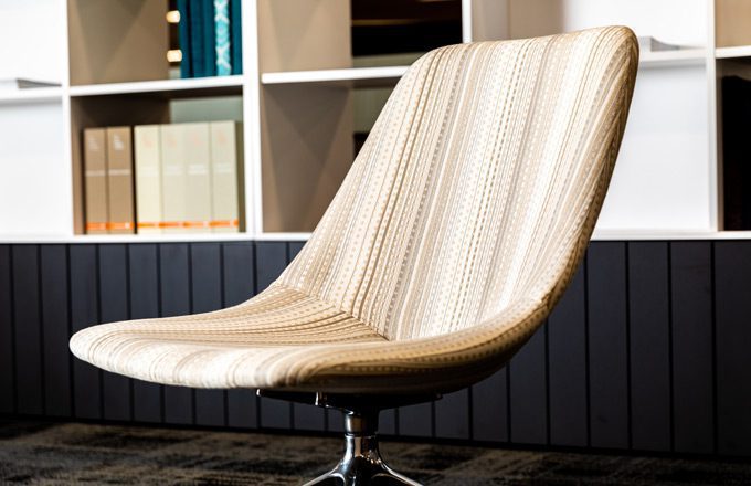 A sleek, modern brown upholstery chair sits in a library