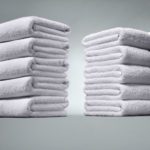 Two stacks of folded bath towels on a grey background.