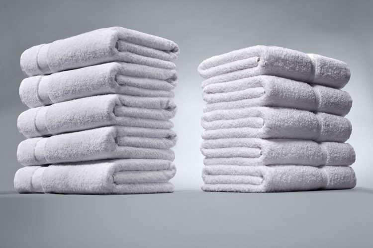 Two stacks of folded bath towels on a grey background.