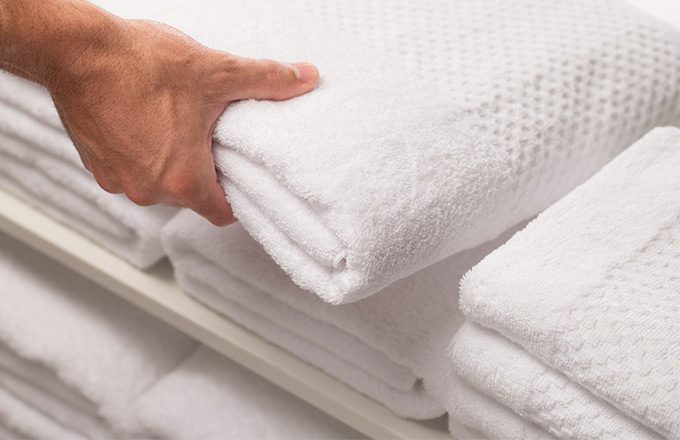 A hand grabs a folded white towel from a shelf full of folded towels.