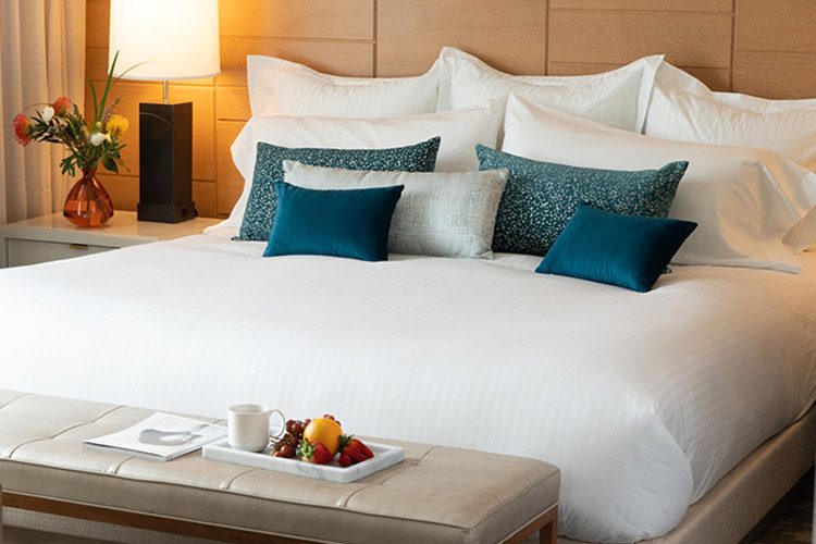 A luxuriously made hotel bed featuring crisp white sheeting, and piles of comfy pillows.