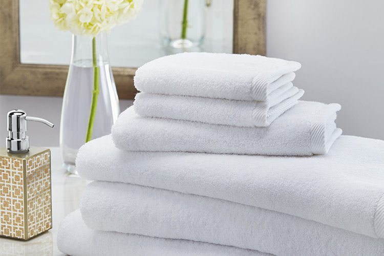 A folded stack of bath towels, hand towels, and wash cloths laying on a bathroom counter.