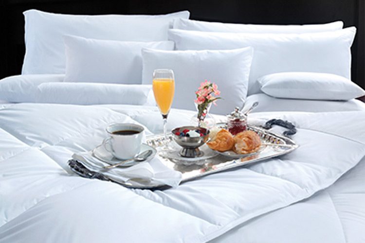 A silver tray of various breakfast foods rests on a well-made hotel bed.