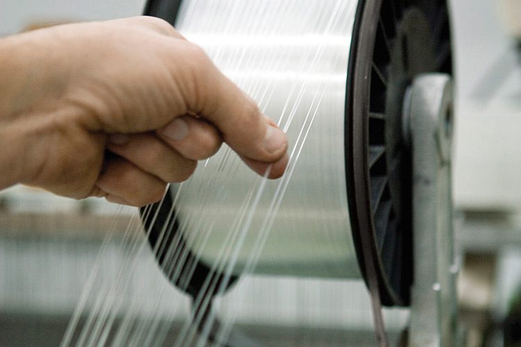 A hand pinches several threads of yarn as they unwind from a spool.