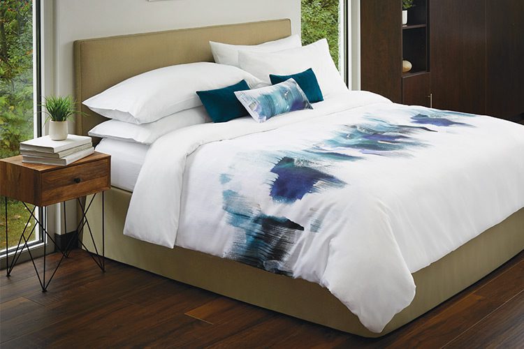 A fully made hotel bed featuring decorative pillows and a custom printed duvet cover.