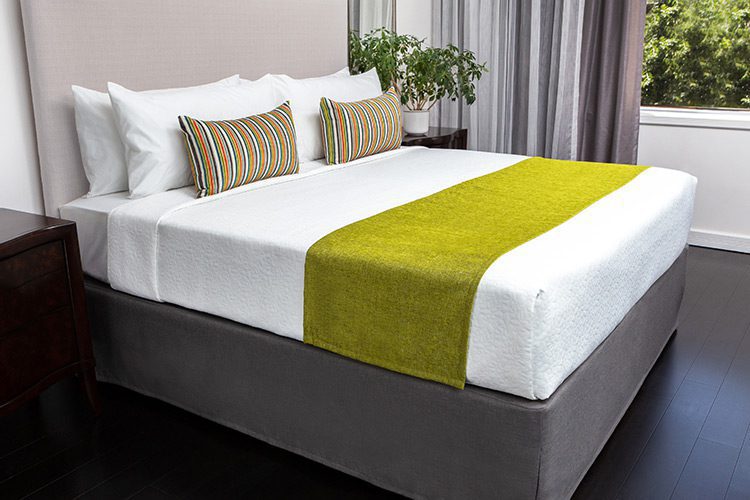 A hotel bed bade with custom bed scarf and decorative throw pillows.