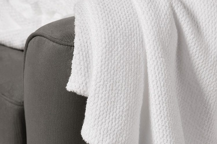 A Lynova wholesale blankets for hotels draped over the arm of a sofa.