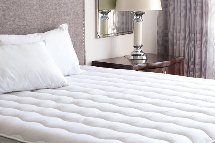 An unmade hotel bed featuring two pillows and a mattress pad.