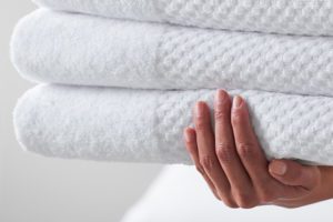 A hand holding a stack of three folded bath towels.